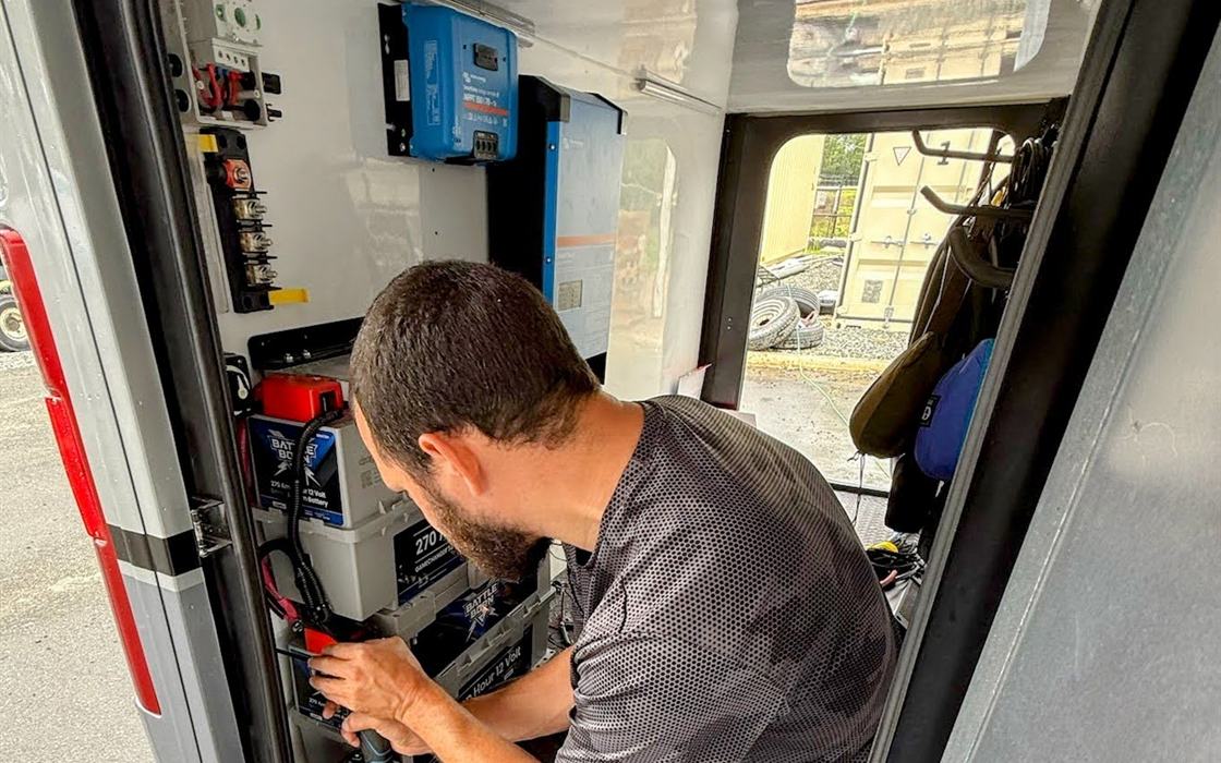 Stream RV technician installing lithium batteries and Victron electronics in an RV compartment
