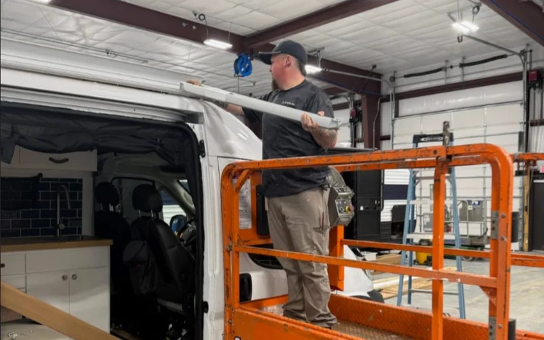 A Stream RV technician working on the roof of a van from a lift in the shop